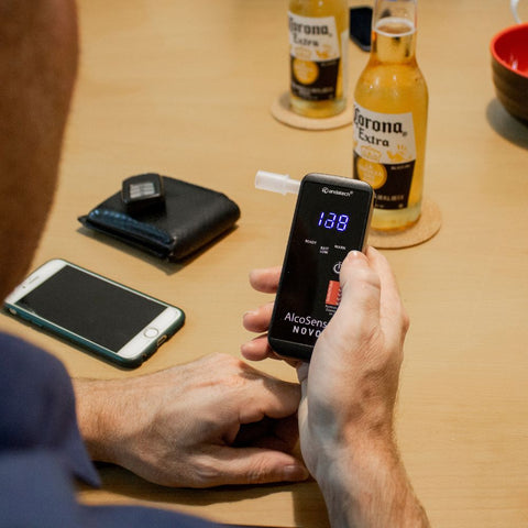 A man Andatech AlcoSense Novo Personal Breathalyser while drinking beer